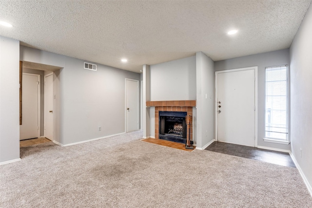 unfurnished living room with carpet, recessed lighting, a tiled fireplace, a textured ceiling, and baseboards