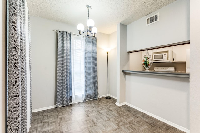 unfurnished dining area featuring visible vents, a notable chandelier, a textured ceiling, and baseboards