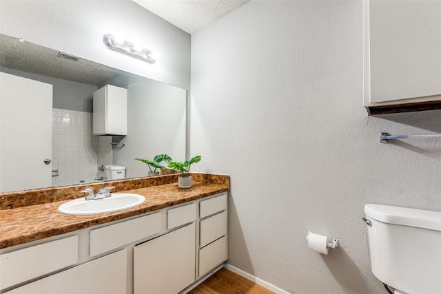 bathroom with a textured ceiling, toilet, wood finished floors, vanity, and baseboards