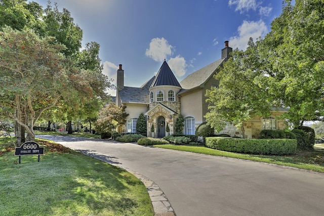 french country inspired facade with stone siding, driveway, stucco siding, a front lawn, and a chimney