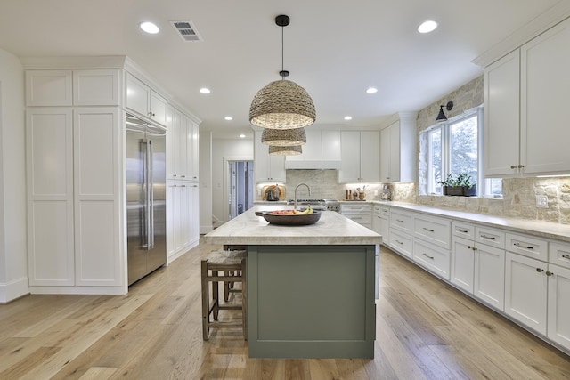 6600 Sahalee Dr, Fort Worth, TX 76132 - kitchen with built in refrigerator, white cabinetry, backsplash, a center island with sink, and hanging light fixtures