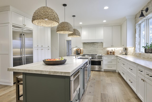 kitchen with light wood-style floors, custom range hood, white cabinetry, and built in appliances