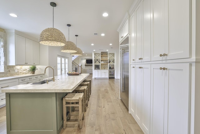 kitchen featuring light wood finished floors, white cabinets, light countertops, a sink, and built in fridge