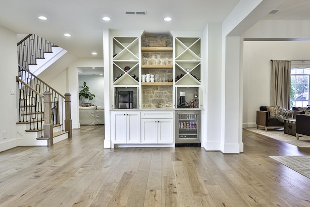 bar with visible vents, a bar, wine cooler, stairway, and light wood-type flooring