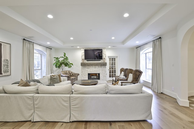 living area featuring light wood-style floors, a fireplace, arched walkways, and a raised ceiling