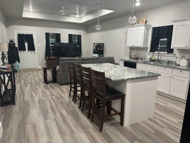 kitchen with light wood finished floors, a kitchen island, a tray ceiling, white cabinetry, and a sink