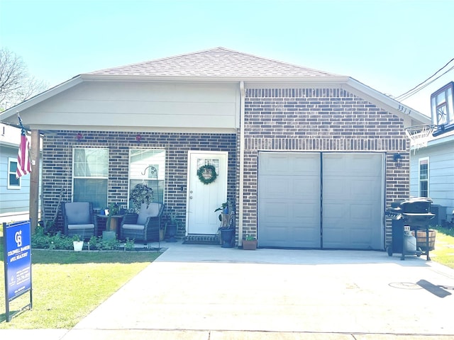 view of front of property with concrete driveway, roof with shingles, brick siding, and a front yard