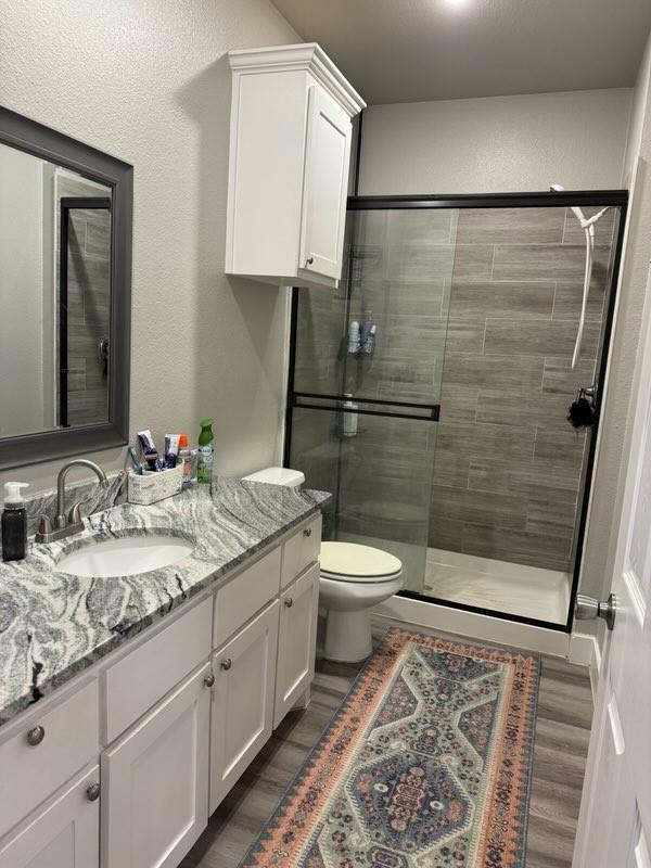 bathroom featuring a shower stall, wood finished floors, vanity, and toilet
