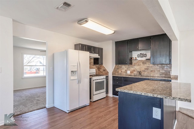 kitchen with under cabinet range hood, white appliances, visible vents, light wood-style floors, and tasteful backsplash