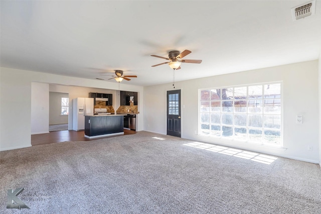 unfurnished living room featuring visible vents, dark carpet, baseboards, and ceiling fan