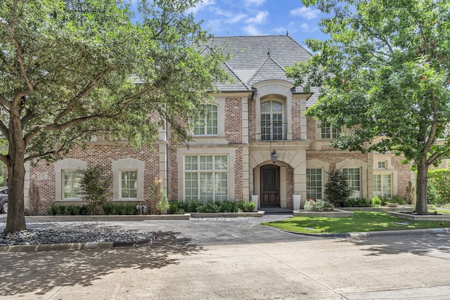 french country inspired facade featuring brick siding and a high end roof