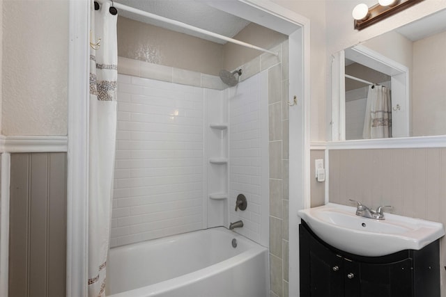 full bath with a textured wall, wainscoting, shower / bath combo with shower curtain, and vanity