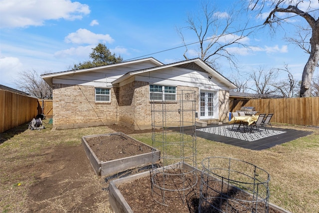 rear view of property with a fenced backyard, brick siding, a garden, french doors, and a lawn