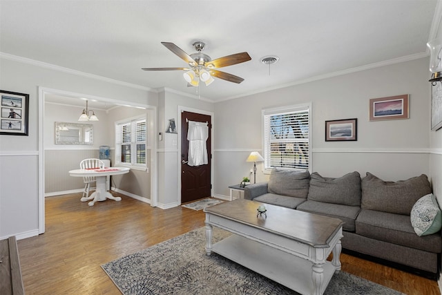 living area with baseboards, visible vents, a ceiling fan, ornamental molding, and wood finished floors