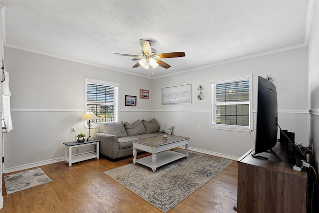 living room featuring ornamental molding, wood finished floors, a ceiling fan, and baseboards