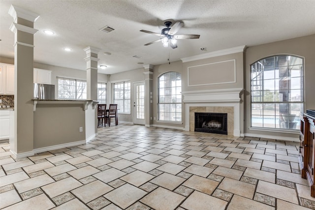 unfurnished living room with baseboards, visible vents, a ceiling fan, a tile fireplace, and ornate columns