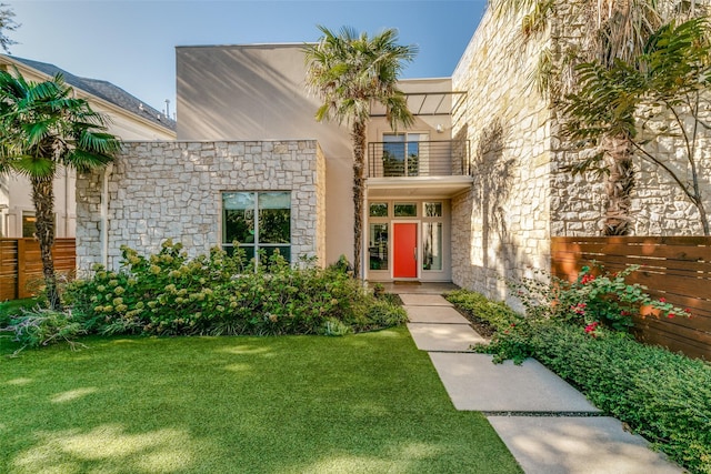 view of exterior entry featuring stone siding, fence, stucco siding, and a yard