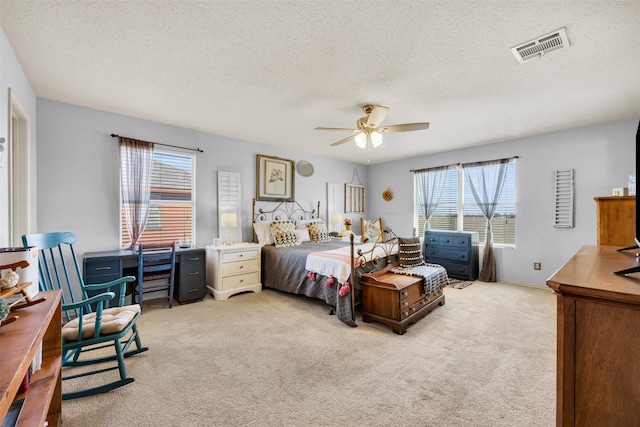 bedroom featuring a ceiling fan, visible vents, a textured ceiling, and light colored carpet