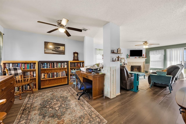 office space featuring visible vents, a tiled fireplace, ceiling fan, wood finished floors, and a textured ceiling