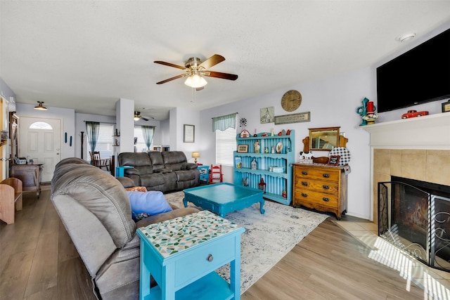 living room featuring ceiling fan, a textured ceiling, a tiled fireplace, and wood finished floors