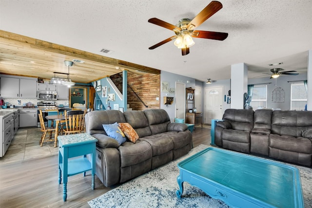 living room with visible vents, a ceiling fan, a textured ceiling, light wood-type flooring, and stairs