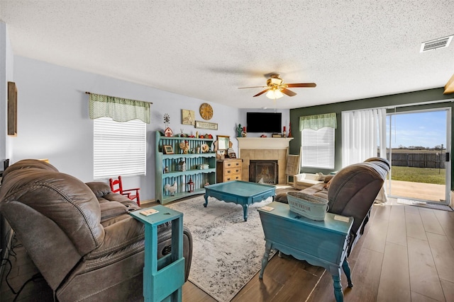 living room featuring a tile fireplace, visible vents, ceiling fan, and wood finished floors