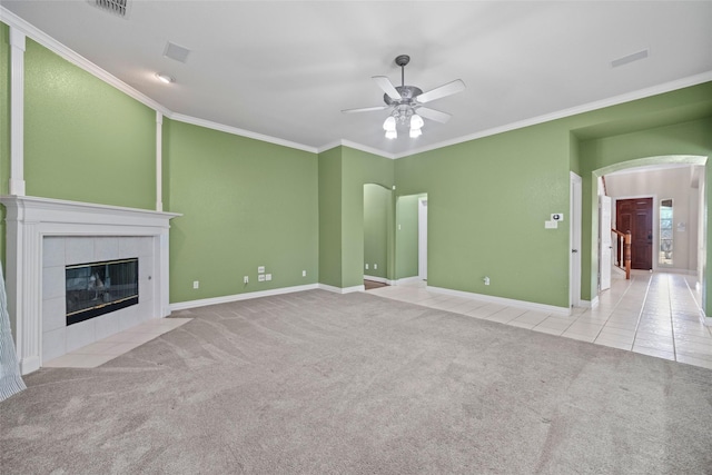 unfurnished living room with crown molding, a tiled fireplace, arched walkways, and carpet flooring