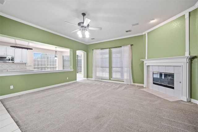 unfurnished living room with light carpet, baseboards, a tile fireplace, ceiling fan, and ornamental molding