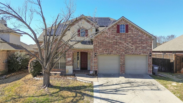 traditional-style house with a garage, solar panels, brick siding, fence, and concrete driveway