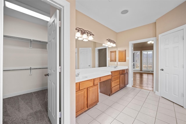 bathroom featuring a sink, baseboards, a spacious closet, tile patterned floors, and double vanity