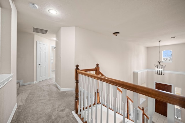 hallway featuring baseboards, visible vents, an inviting chandelier, carpet flooring, and an upstairs landing