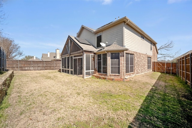 rear view of house featuring a fenced backyard, solar panels, brick siding, a sunroom, and a yard