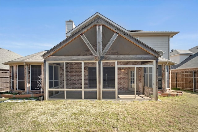 rear view of property featuring brick siding, a lawn, fence, and a sunroom