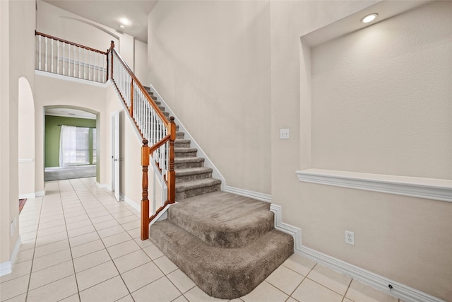 staircase with tile patterned flooring, a high ceiling, arched walkways, and baseboards