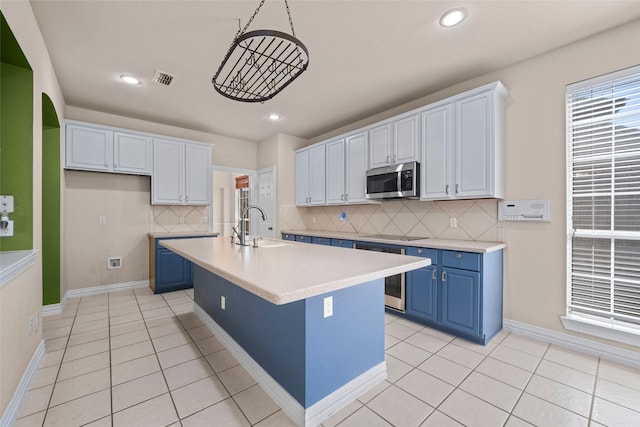 kitchen featuring stainless steel microwave, light countertops, blue cabinetry, a sink, and light tile patterned flooring