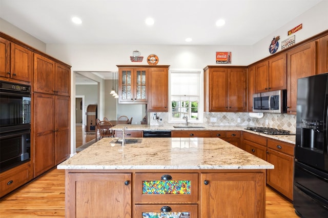 kitchen featuring a center island with sink, light stone counters, a sink, black appliances, and backsplash