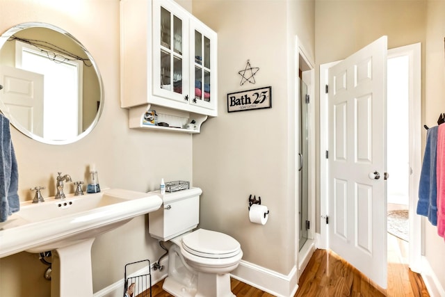 bathroom with a stall shower, baseboards, toilet, wood finished floors, and a sink