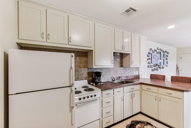 kitchen featuring dark countertops, visible vents, decorative backsplash, a sink, and white appliances