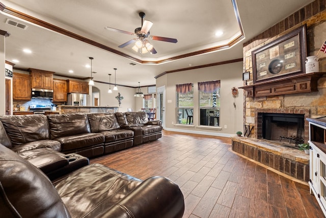 living area with a fireplace, a raised ceiling, visible vents, dark wood-type flooring, and ornamental molding