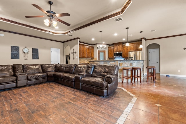 living room featuring arched walkways, visible vents, baseboards, a raised ceiling, and crown molding