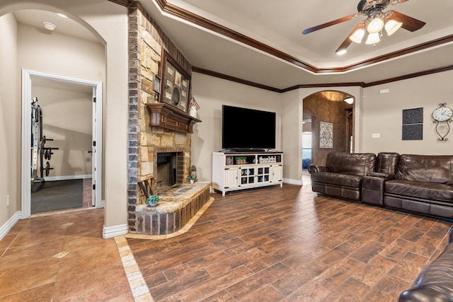 living area featuring arched walkways, a fireplace, a raised ceiling, ornamental molding, and baseboards