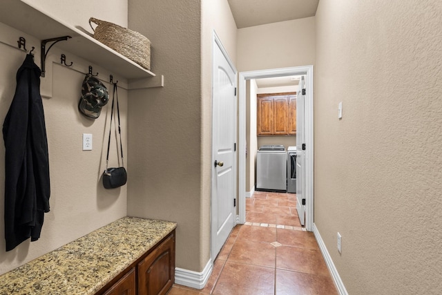 mudroom featuring light tile patterned floors, a textured wall, washing machine and dryer, and baseboards