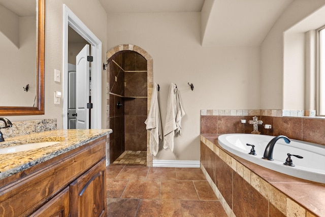 bathroom featuring baseboards, stone finish floor, vanity, a walk in shower, and a bath