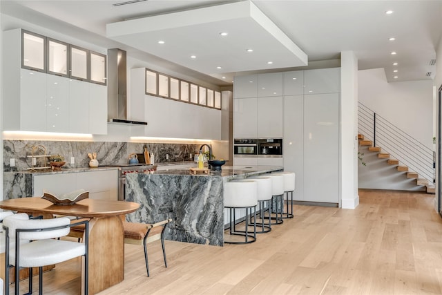 kitchen featuring a breakfast bar, white cabinetry, wall chimney exhaust hood, and modern cabinets