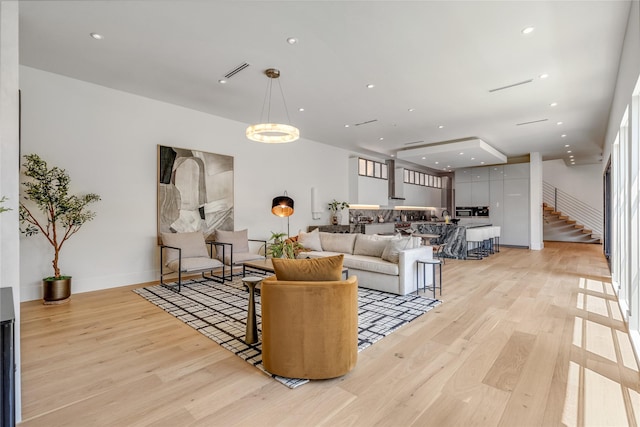 living room featuring light wood-style floors, visible vents, stairs, and a chandelier