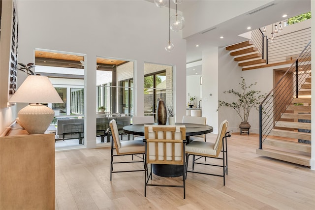 dining room with stairs, light wood-type flooring, a towering ceiling, and visible vents