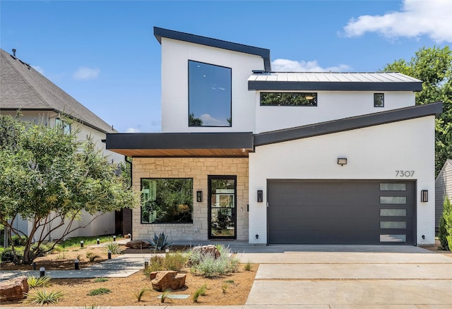 contemporary home with driveway, stone siding, metal roof, a standing seam roof, and stucco siding