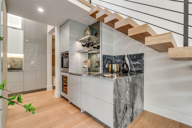 bar featuring wine cooler, a sink, stainless steel oven, light wood-style floors, and backsplash