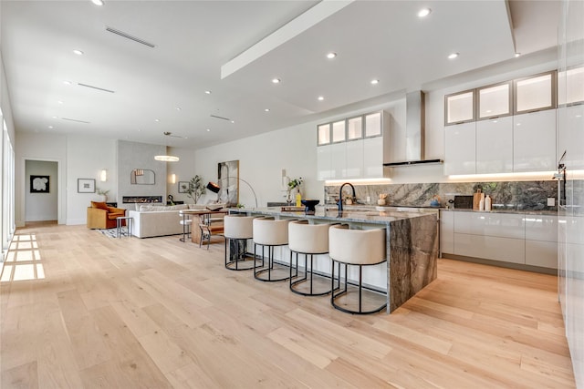 kitchen featuring an island with sink, wall chimney range hood, modern cabinets, and white cabinetry