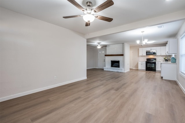 unfurnished living room with ceiling fan with notable chandelier, visible vents, baseboards, light wood-style floors, and a brick fireplace